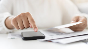 woman holding a paper bill invoice and using a smartphone