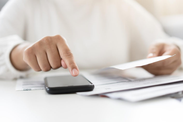 woman holding a paper bill invoice and using a smartphone