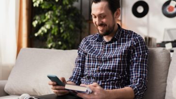 man holding a smartphone and a book