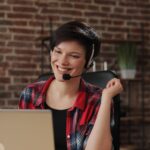 smiling woman with a headset working on a laptop from home