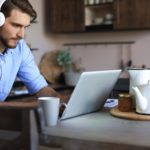 man with headphones working remotely on a laptop from a kitchen