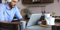 man with headphones working remotely on a laptop from a kitchen