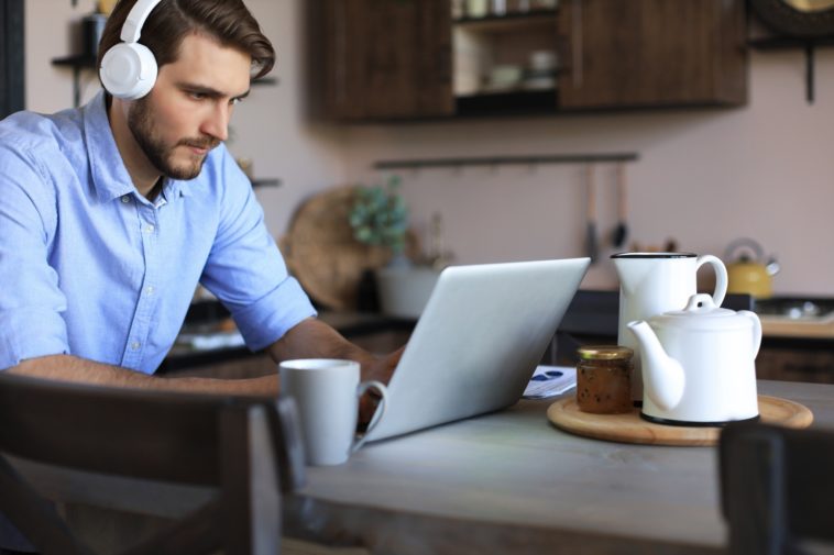 man with headphones working remotely on a laptop from a kitchen