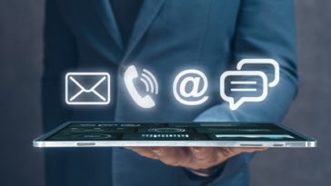 businessman holding a tablet with 3D mail, phone, email and chat icons above it