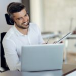 smiling man with headphones using laptop while on a call