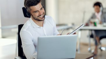 smiling man with headphones using laptop while on a call