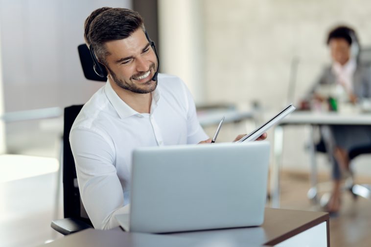 smiling man with headphones using laptop while on a call