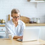 smiling woman working on a laptop from a kitchen