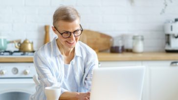 smiling woman working on a laptop from a kitchen