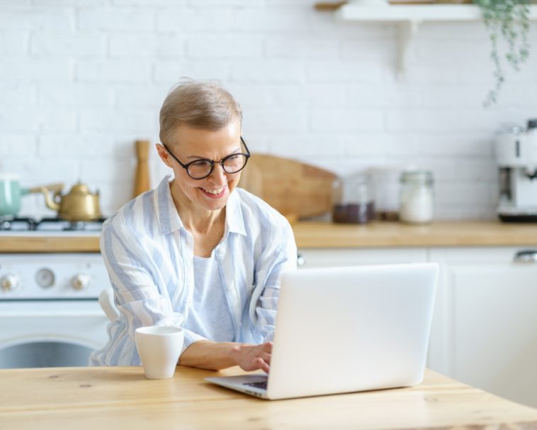 smiling woman working on a laptop from a kitchen