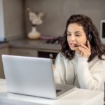 woman speaking on headphones in front of a laptop at home