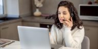 woman speaking on headphones in front of a laptop at home