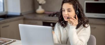 woman speaking on headphones in front of a laptop at home