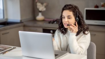 woman speaking on headphones in front of a laptop at home