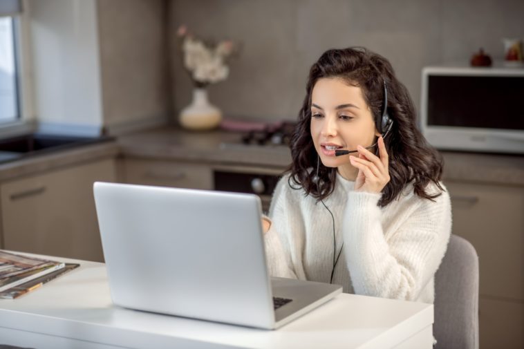 woman speaking on headphones in front of a laptop at home