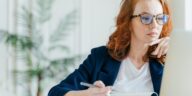 woman looking at a computer making notes in a notepad