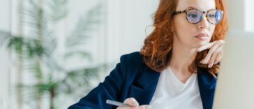 woman looking at a computer making notes in a notepad