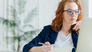 woman looking at a computer making notes in a notepad