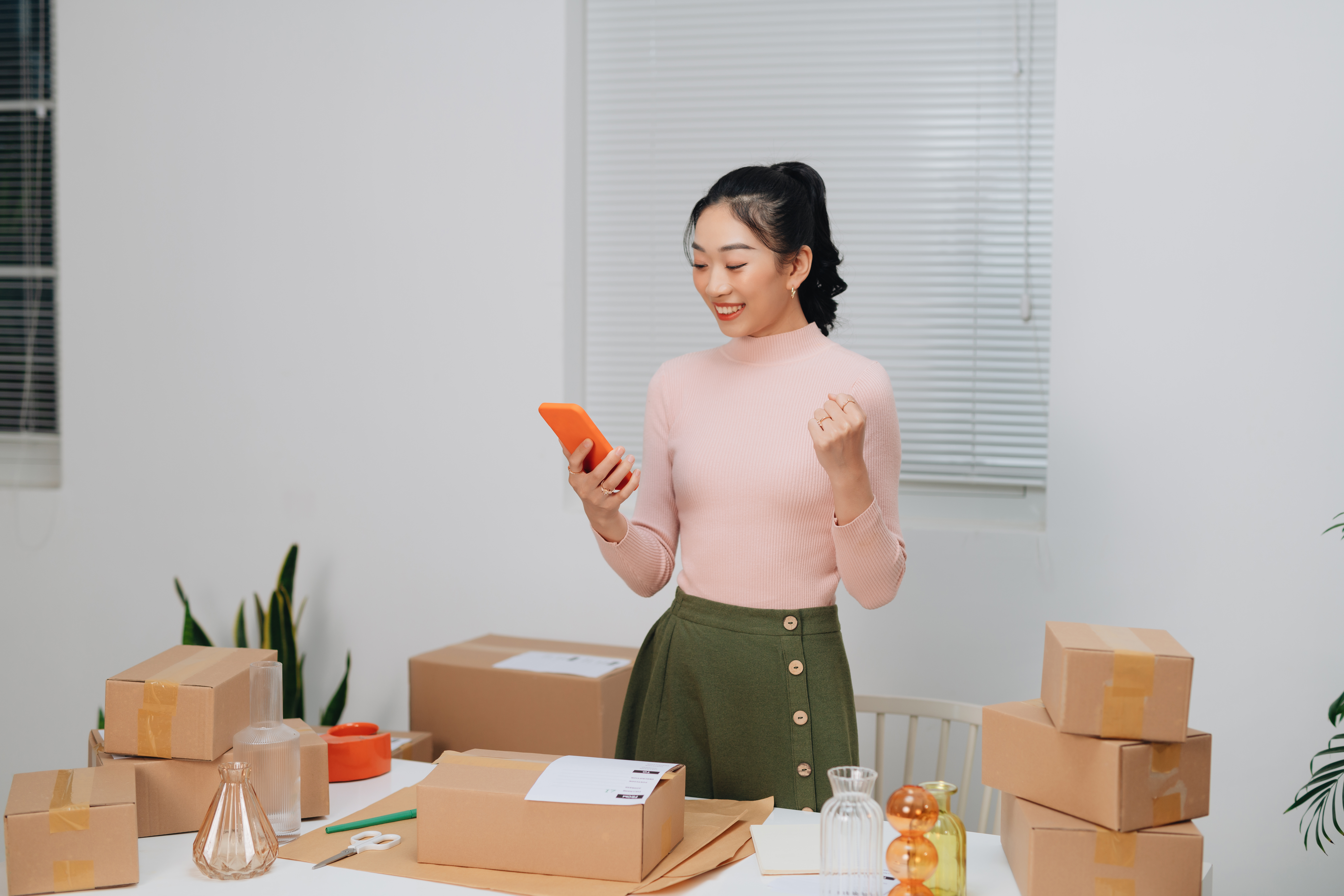 woman surrounded by boxes looking at her phone smiling