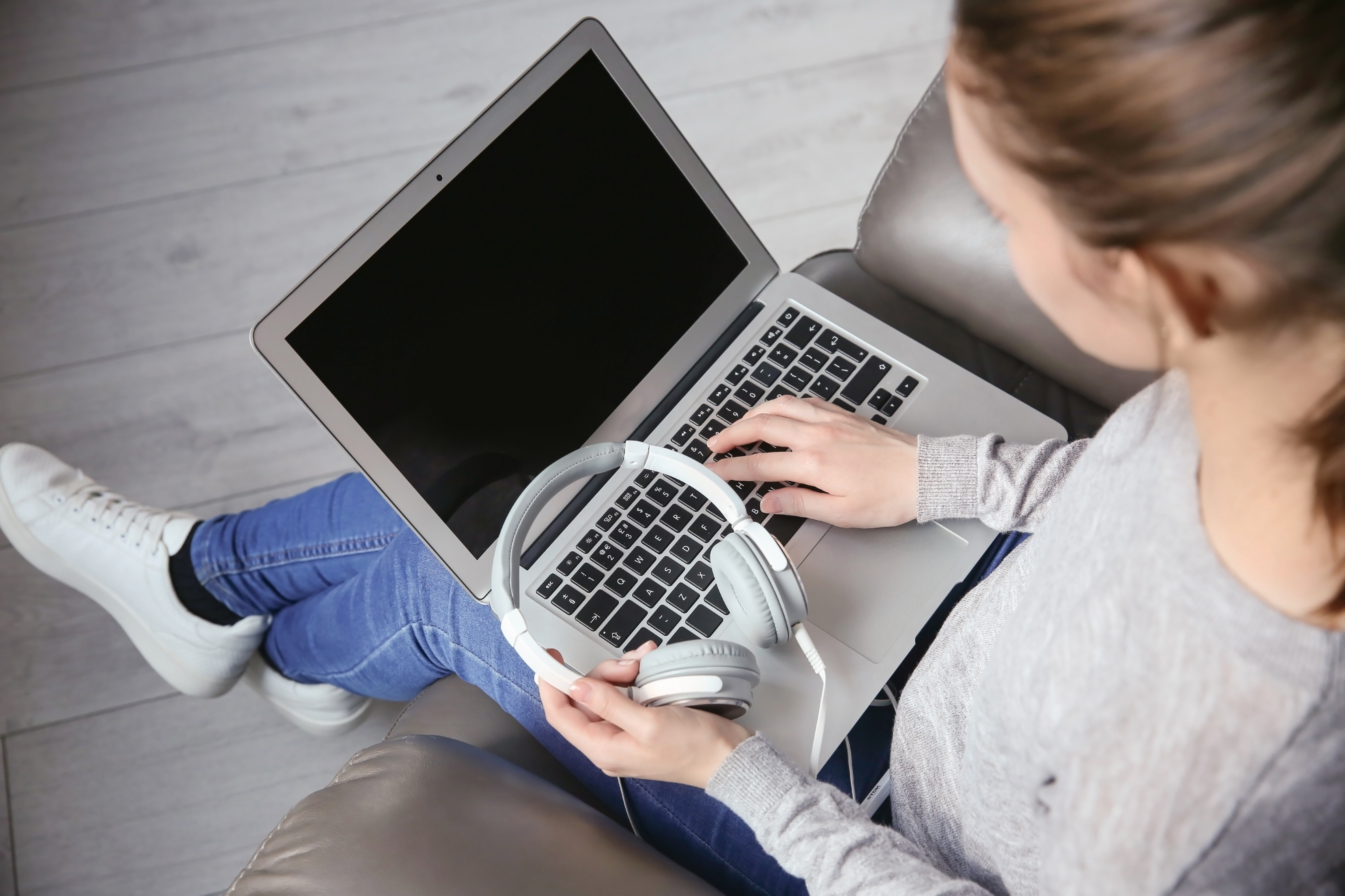 woman sitting on a sofa holding a laptop and headphones