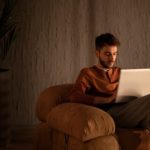 man sitting in a sofa chair working on a laptop