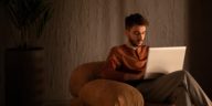 man sitting in a sofa chair working on a laptop