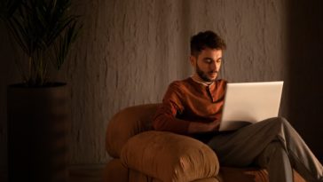 man sitting in a sofa chair working on a laptop