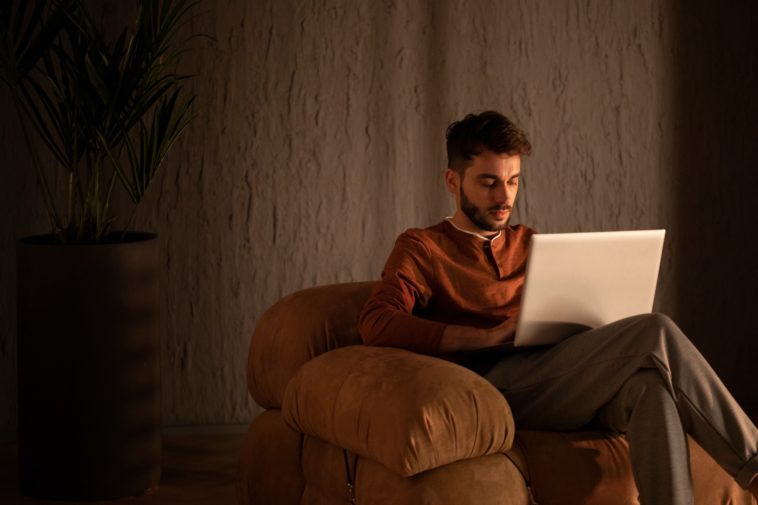 man sitting in a sofa chair working on a laptop