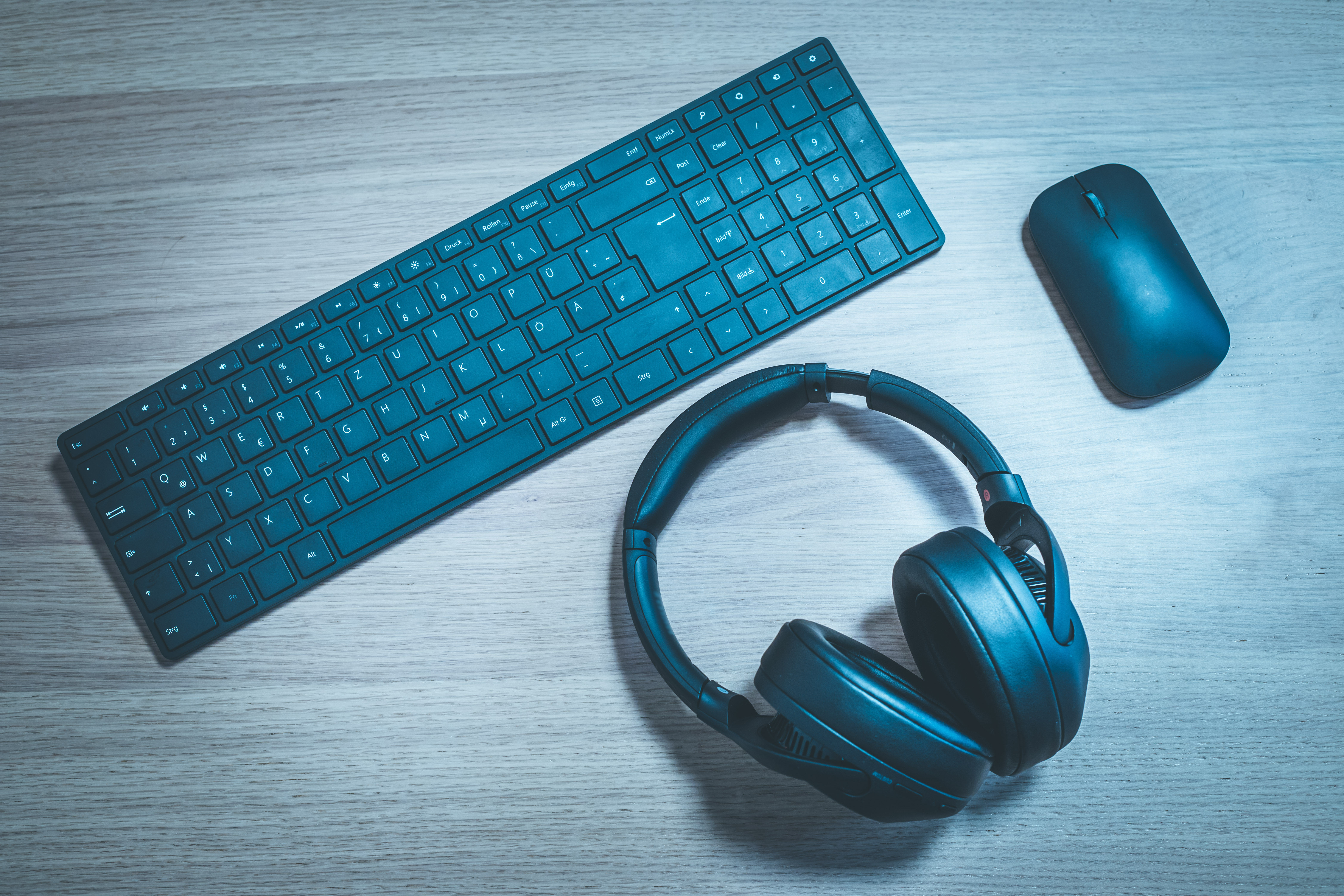 a black keyboard, headphones and a mouse on a wooden desk