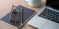 work desk with a laptop, notebook, pencil, glasses and coffee mug