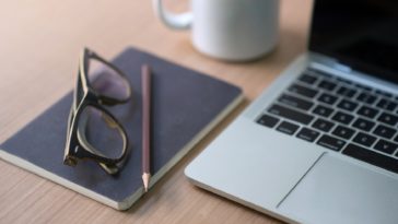 work desk with a laptop, notebook, pencil, glasses and coffee mug