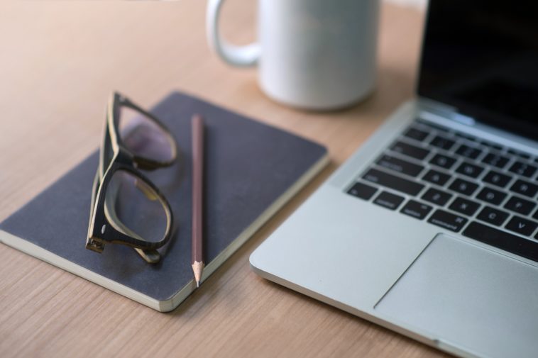 work desk with a laptop, notebook, pencil, glasses and coffee mug