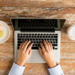 female hands typing on a laptop with coffee and cookies next to it