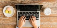 female hands typing on a laptop with coffee and cookies next to it