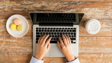 female hands typing on a laptop with coffee and cookies next to it