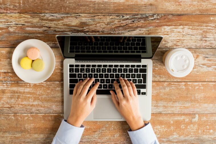 female hands typing on a laptop with coffee and cookies next to it