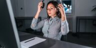 woman sitting at a desk with a computer putting on a headset