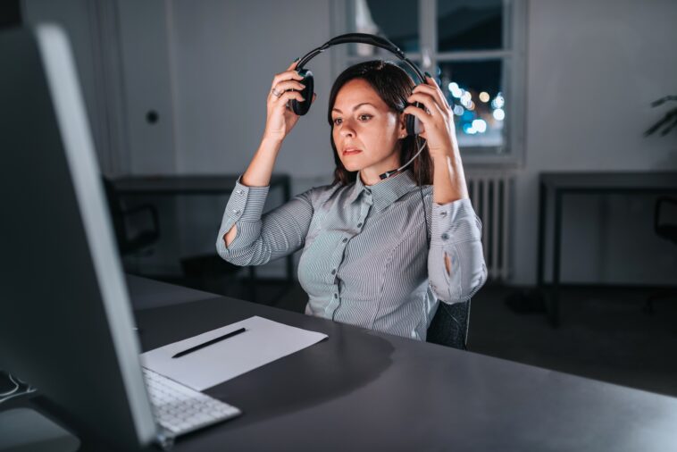 woman sitting at a desk with a computer putting on a headset