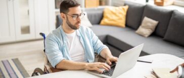 man in a wheelchair working on a laptop from home