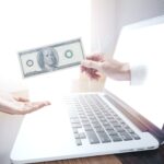 hand coming out of a computer screen handing a dollar bill to another hand