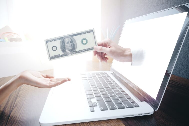 hand coming out of a computer screen handing a dollar bill to another hand