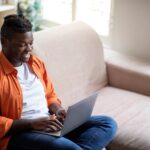 man sitting on a couch working on a laptop from home