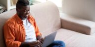 man sitting on a couch working on a laptop from home