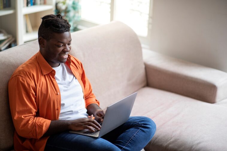 man sitting on a couch working on a laptop from home