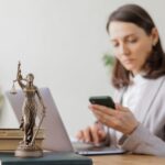 woman sitting in an office looking at her phone with a goddess of justice statuette on the desk
