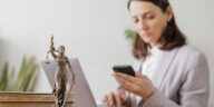 woman sitting in an office looking at her phone with a goddess of justice statuette on the desk