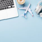 a laptop, model plane, headphones and coffee on a baby blue surface