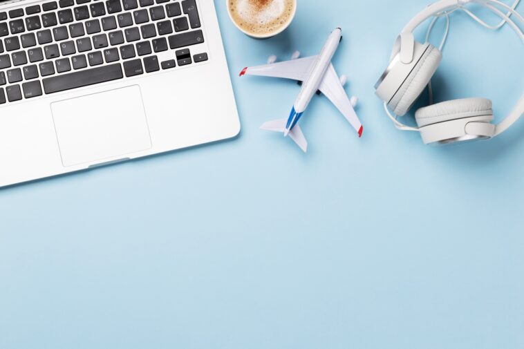 a laptop, model plane, headphones and coffee on a baby blue surface