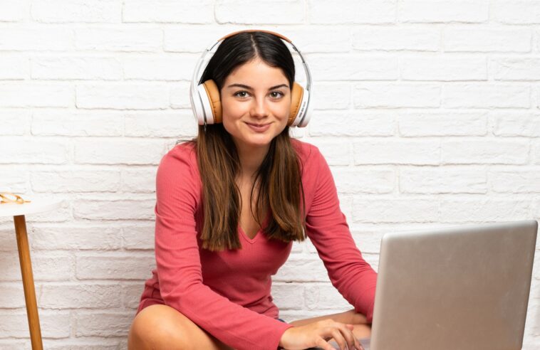 woman with headphones working on a laptop sitting on the floor