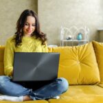 girl working from home on a couch with a laptop in her lap